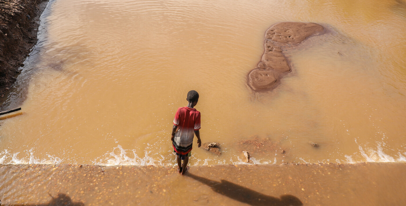 Un bambino cammina accanto a un ponte distrutto a Buna a causa delle inondazioni