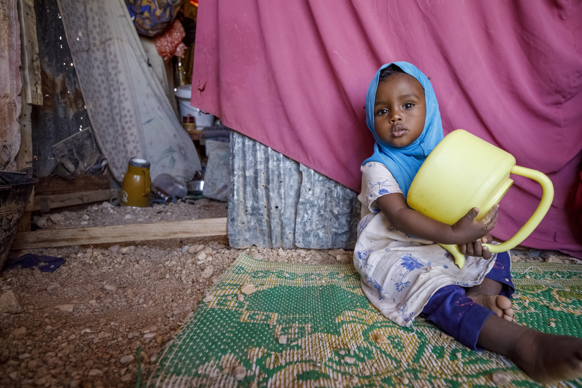 In un campo per sfollati alla periferia di Garowe, alcune famiglie diverse hanno trovato rifugio dopo aver dovuto lasciare le loro case a causa della siccità in corso. Alcune persone vivono qui dall'ultima siccità del 2017. Hafsa Abdikader Ahmed (scrarf dai capelli rossi) ha vent'anni. "Sono arrivata dieci giorni fa dal mio villaggio, mio ​​marito ha portato me e i due bambini in questo campo per sfollati interni vicino a Garowe. Ho due bambini, mia figlia ha un anno e mezzo, mio ​​figlio cinque anni. Dopo che mio marito ci ha portato qui è tornato al villaggio, da allora non ho più notizie di lui. Abbiamo portato con noi due capre, anche se sono molto deboli. Avevamo più di 150 capre, tutte tranne due sono morte a causa della siccità. Il che è devastante per la nostra situazione domestica, le capre producono latte, carne e denaro se le vendiamo. Qui nel campo non riceviamo alcun sostegno. Vorrei che potessimo tornare al nostro villaggio, qui nel campo non c'è niente di cui vivere."